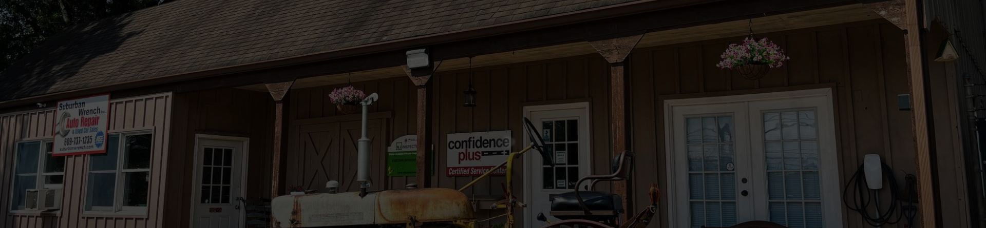 Old wooden storefront with a porch, hanging plants, and a blue door under a dark roof. | Suburban Wrench