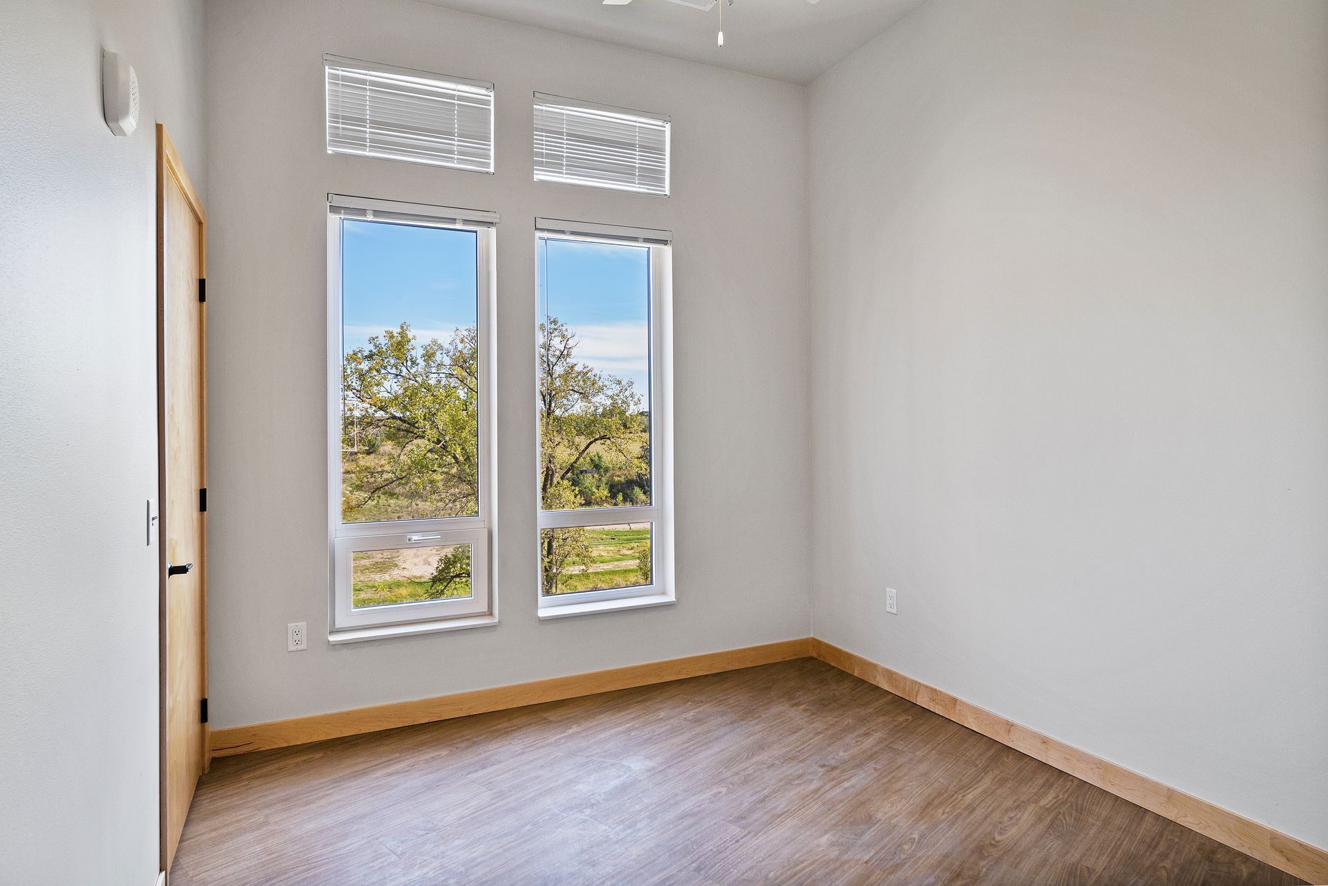 An empty bedroom with two windows and a wooden floor.