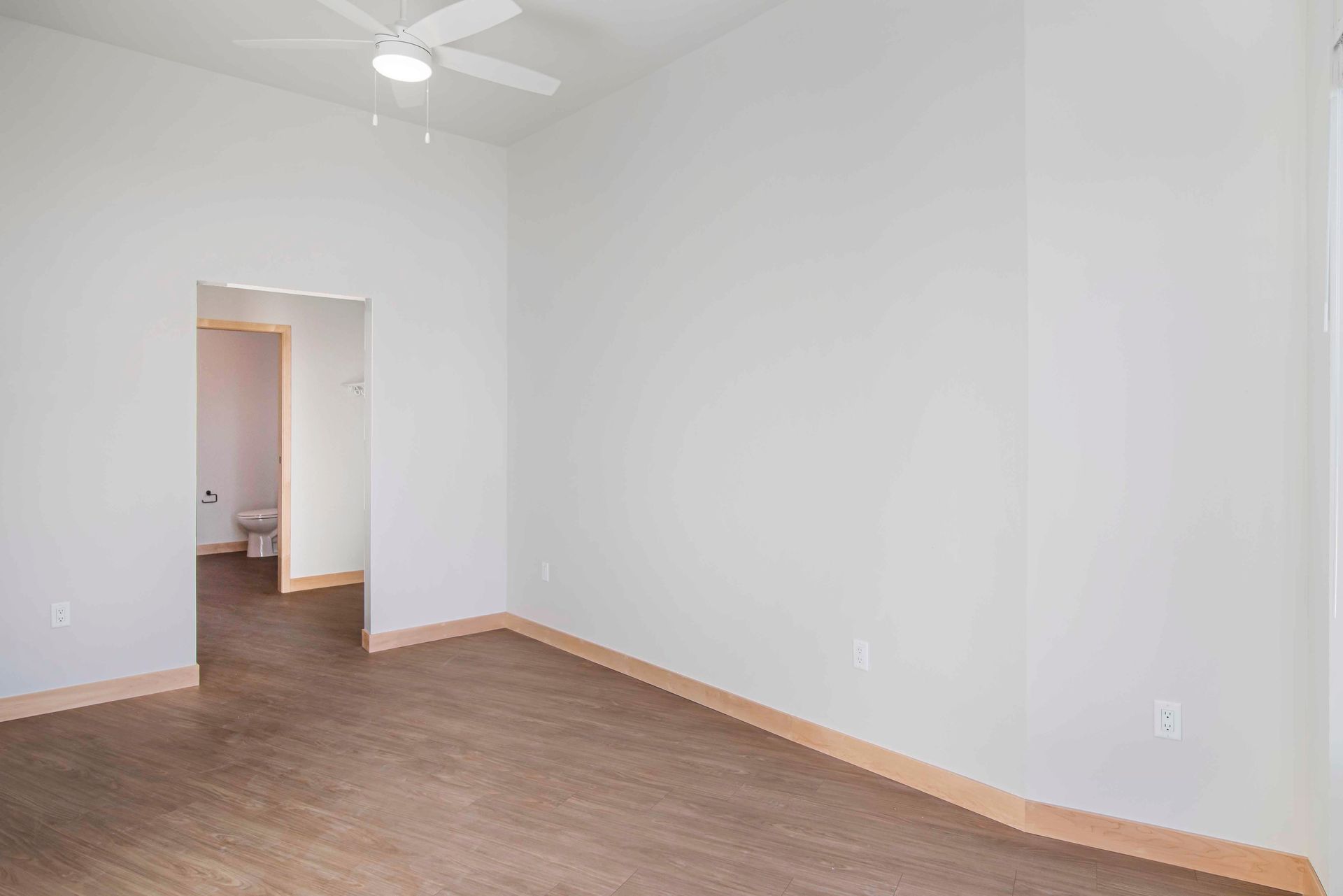 An empty room with a ceiling fan and a bathroom in the background.
