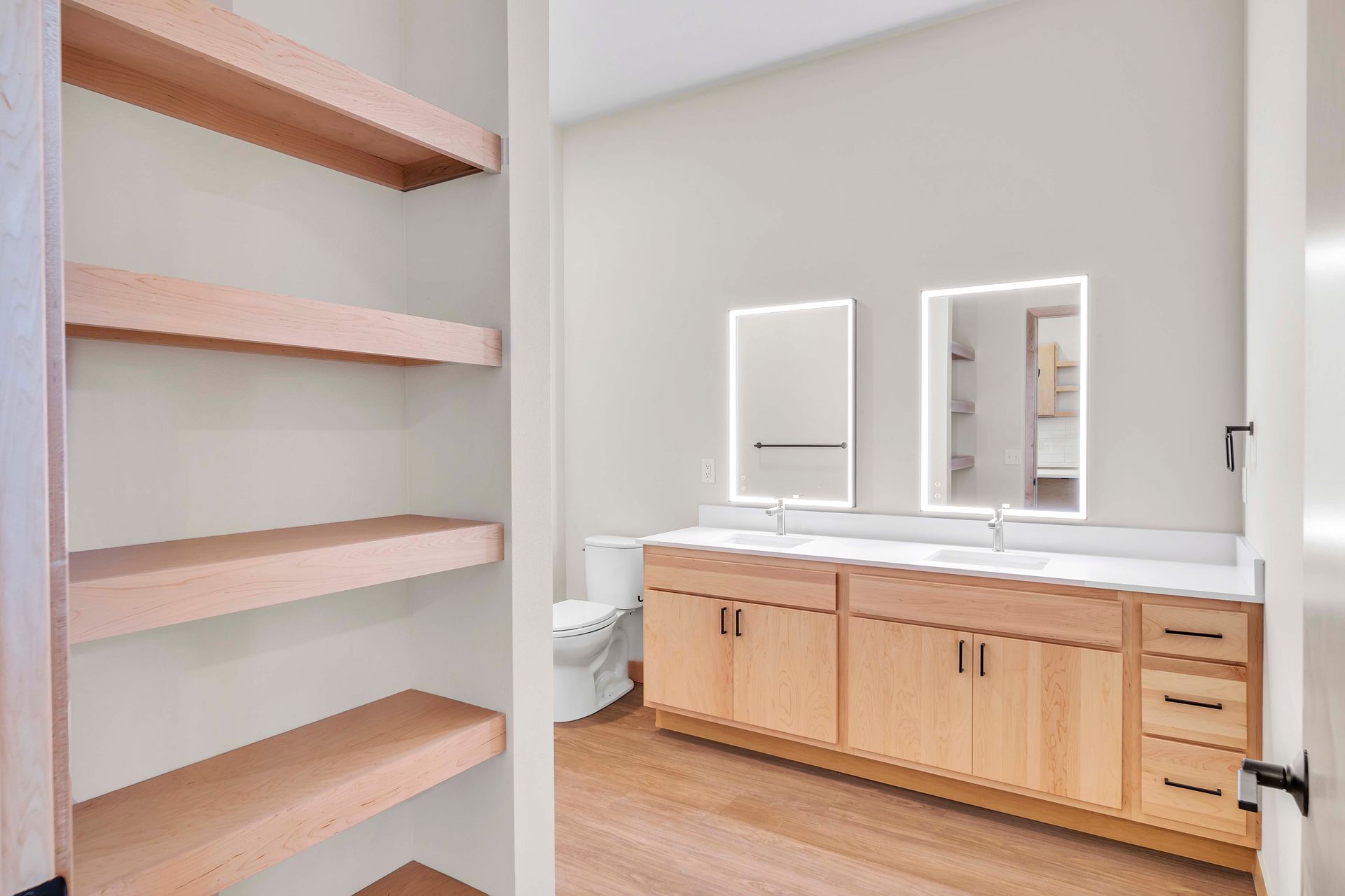 A bathroom with a toilet , sink , mirrors and shelves.