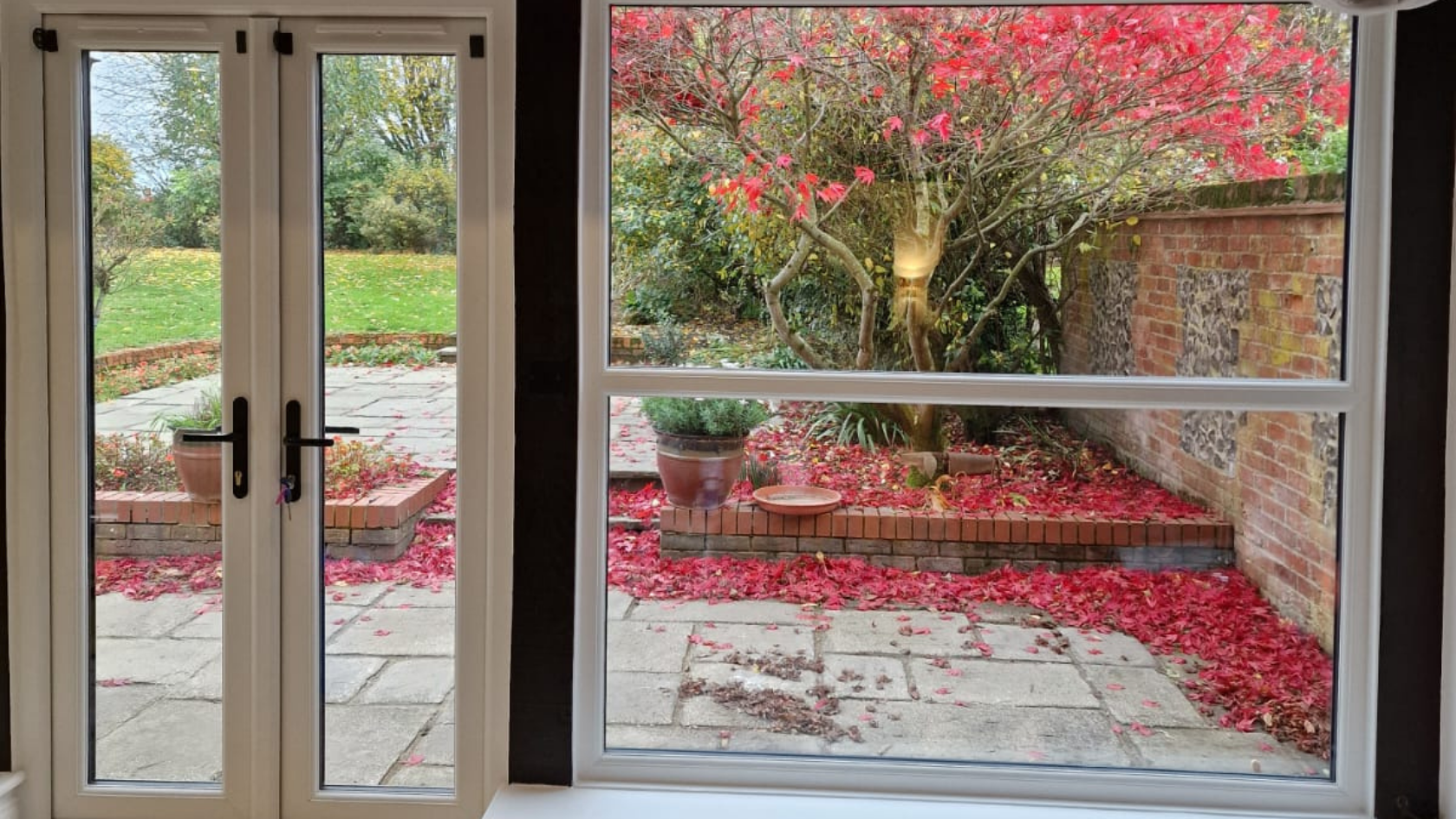 French doors open onto a patio covered in red leaves, with a red-leafed tree and brick wall visible.