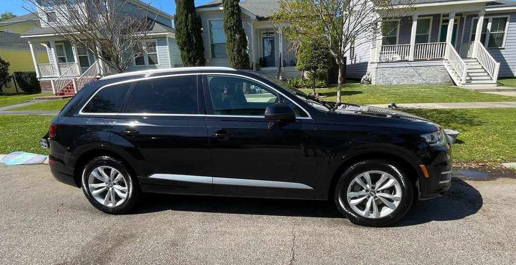 A black audi q7 is parked on the side of the road in front of a house.