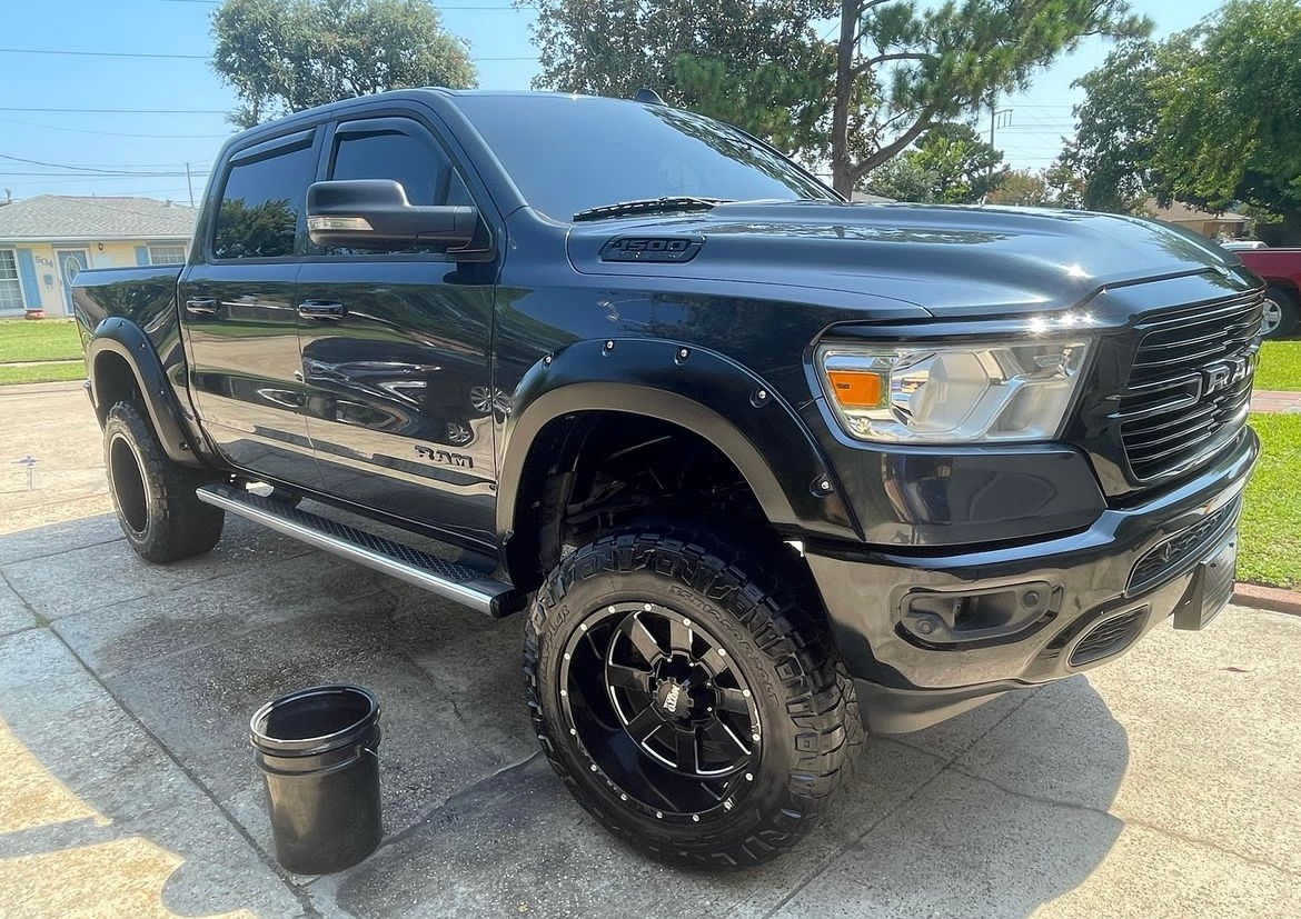 A black dodge ram truck is parked in a driveway next to a bucket.