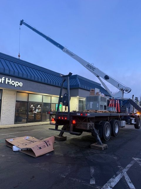 Crane truck lifting equipment outside a storefront at dusk, with cardboard boxes on the ground.
