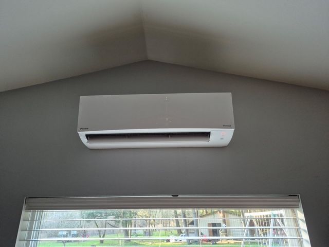 Wall-mounted white air conditioner above a window in a room with a sloped ceiling
