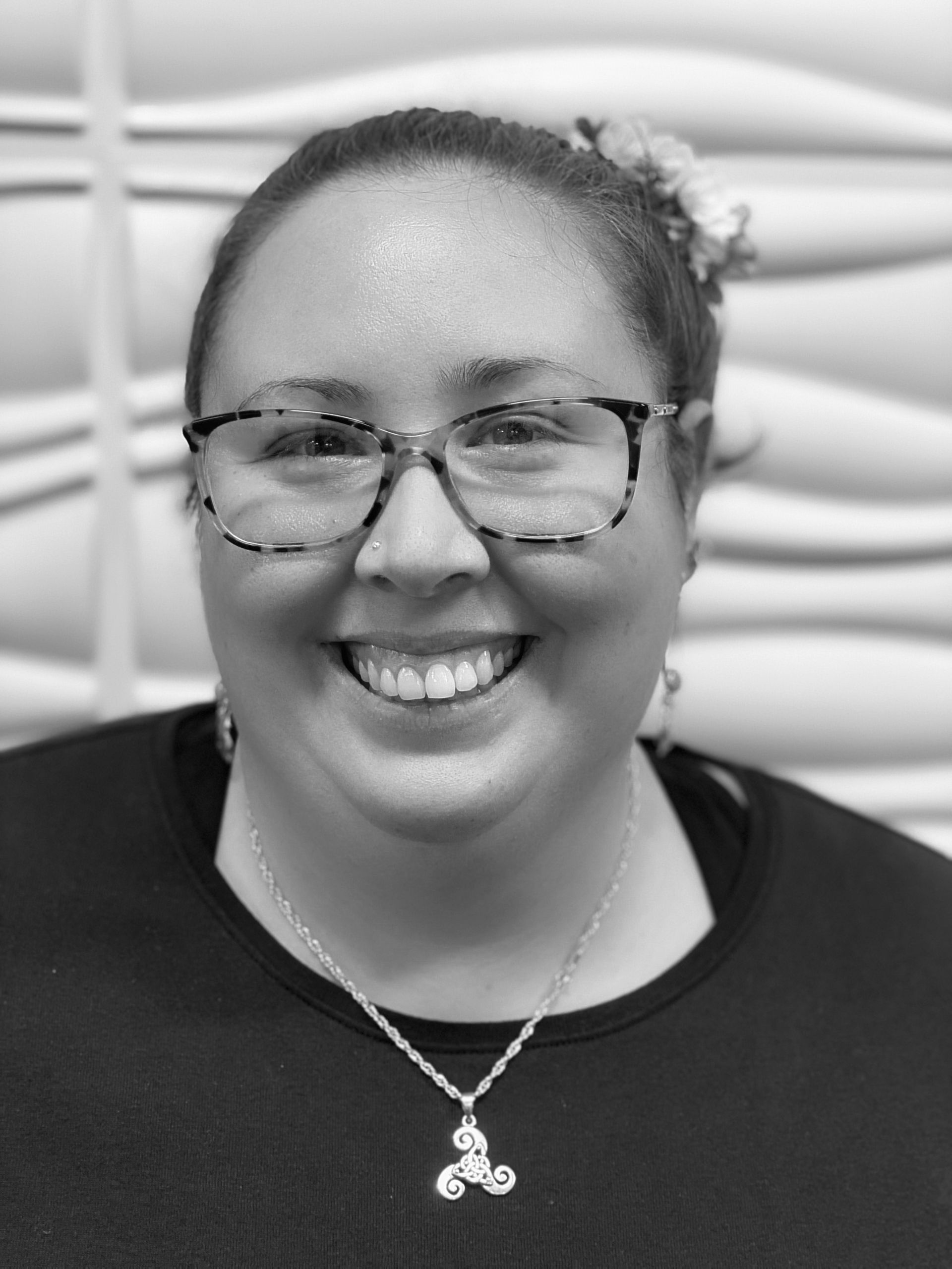 A woman wearing glasses and a necklace is smiling in a black and white photo.