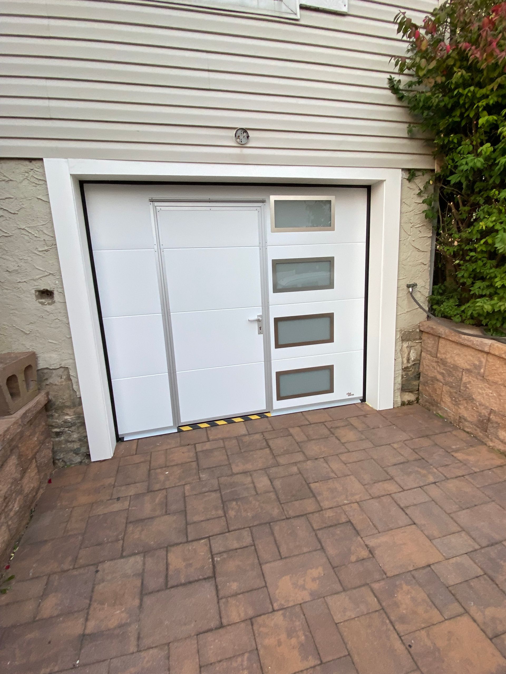 A white garage door is sitting on a brick driveway next to a house.