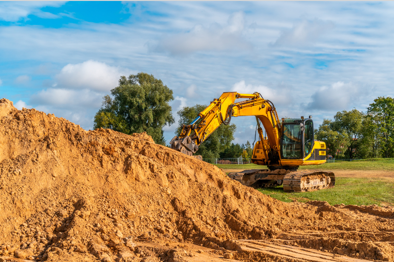 Yellow excavator digging a large dirt mound at a construction site under a blue sky