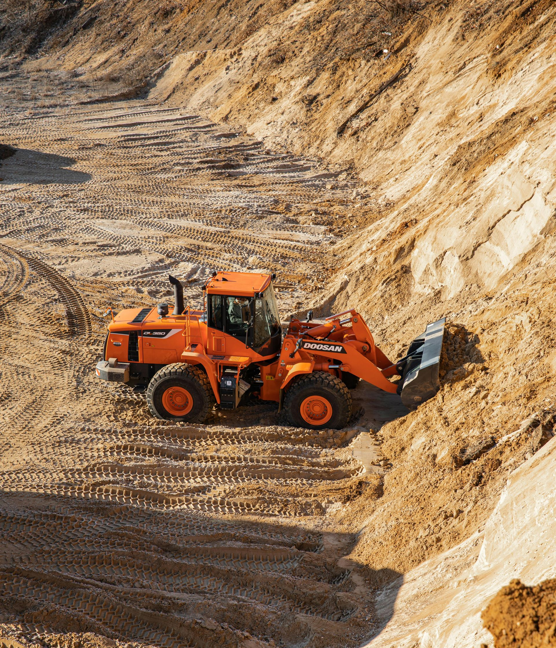Orange front loader working in a rocky quarry, pushing dirt beside a steep sand wall.