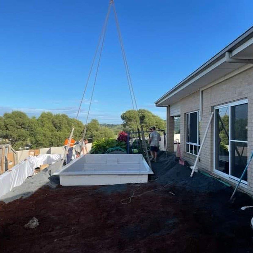 A crane is lifting a swimming pool onto the roof of a house.