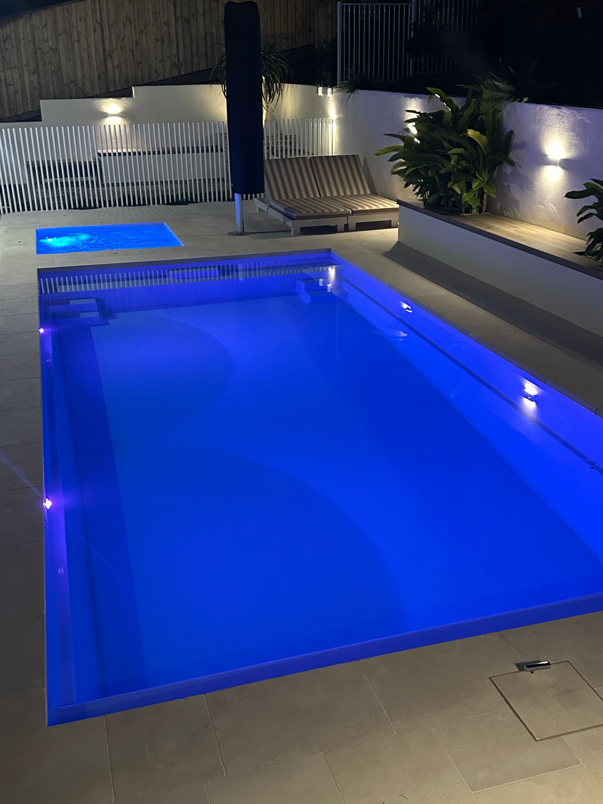 A large swimming pool is lit up at night with blue lights.