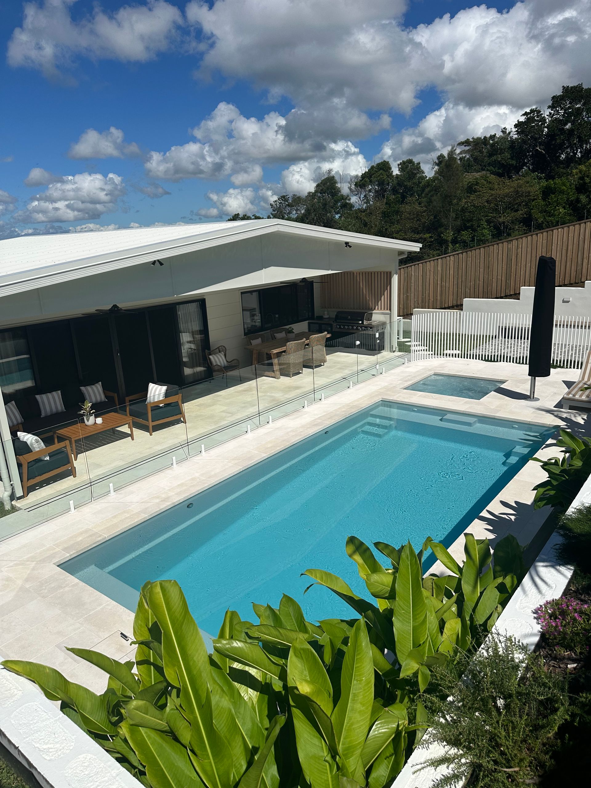 Pool and patio of a white house. Blue water, plants, and a sunny day — Evoke Pools In Lennox Head, NSW