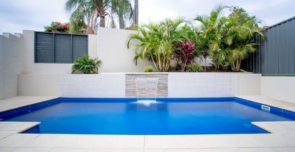 A large swimming pool with a waterfall in the backyard of a house.
