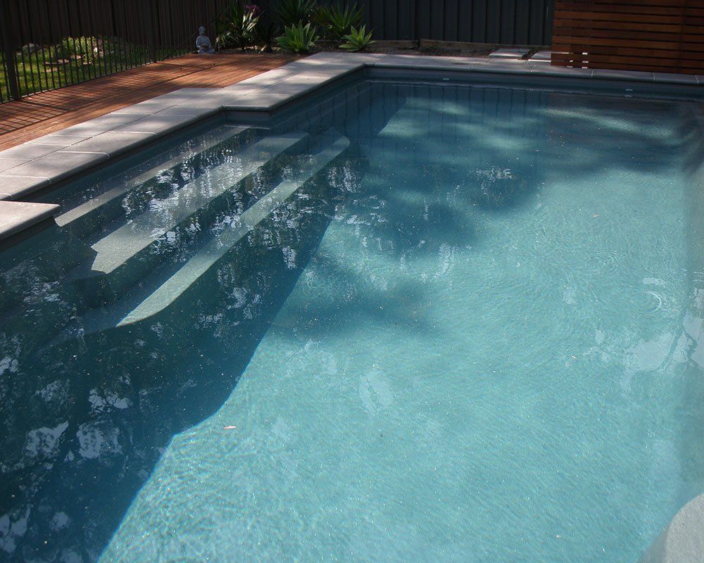 A swimming pool with stairs and a fence in the background