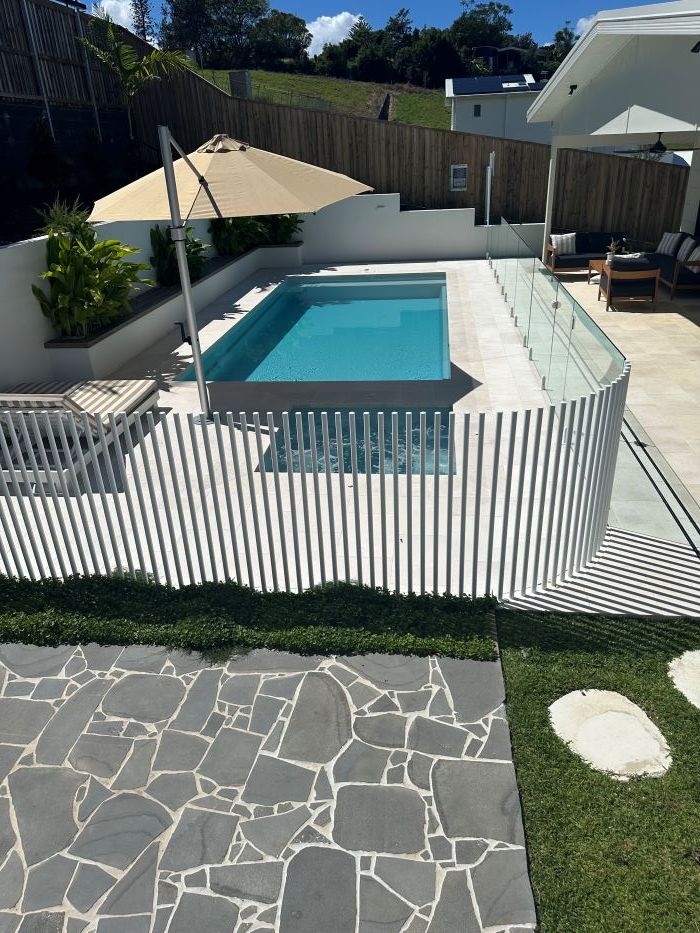 A large swimming pool surrounded by a white fence and umbrellas