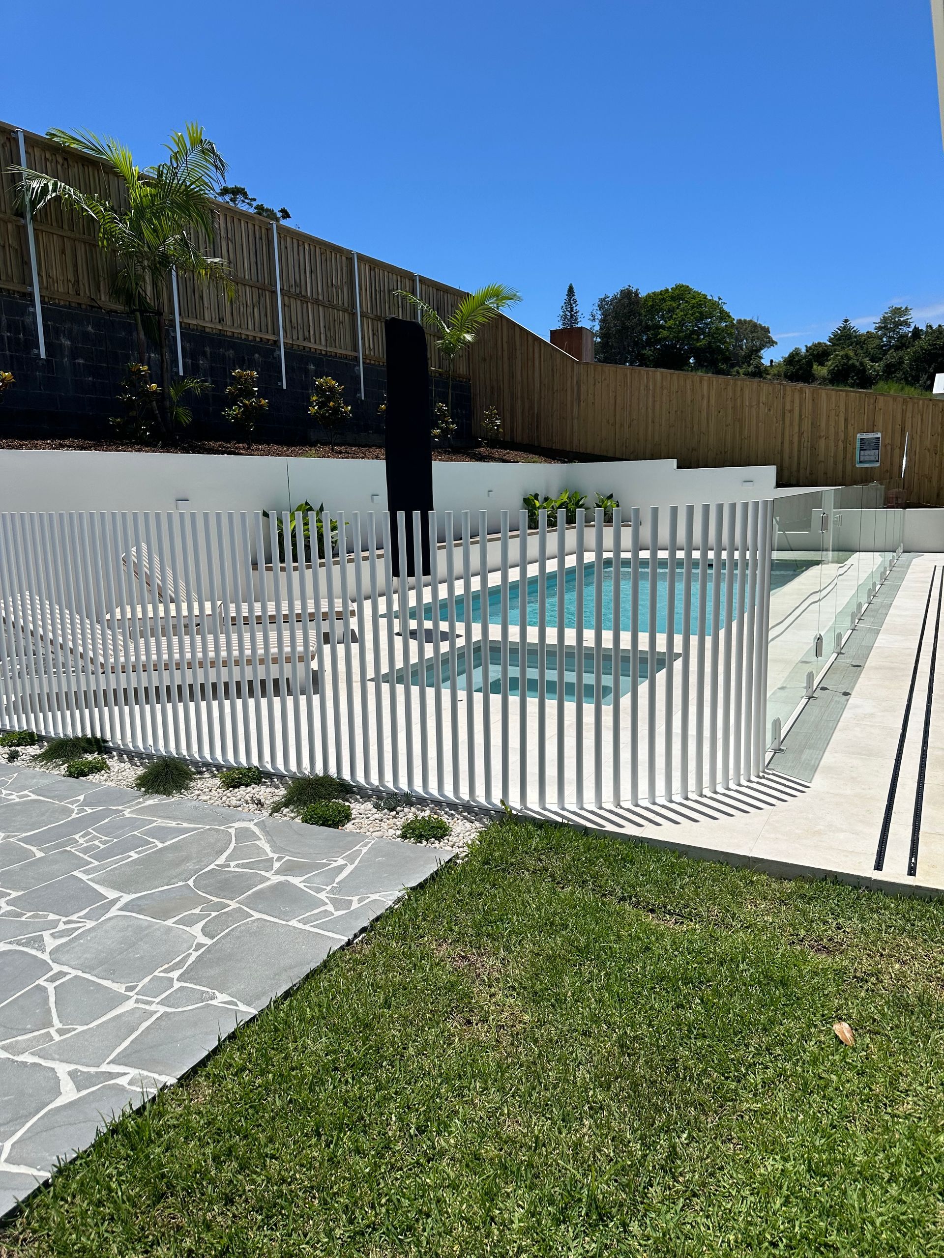 Pool area with white fence, lush grass, stone path, and bamboo backdrop under a blue sky — Evoke Pools In Lennox Head, NSW