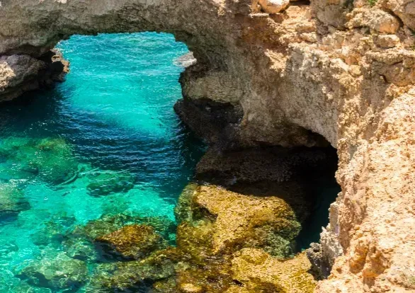 There is a cave in the middle of the ocean surrounded by rocks.
