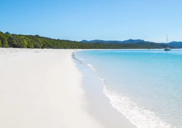 A white sandy beach with a boat in the distance.
