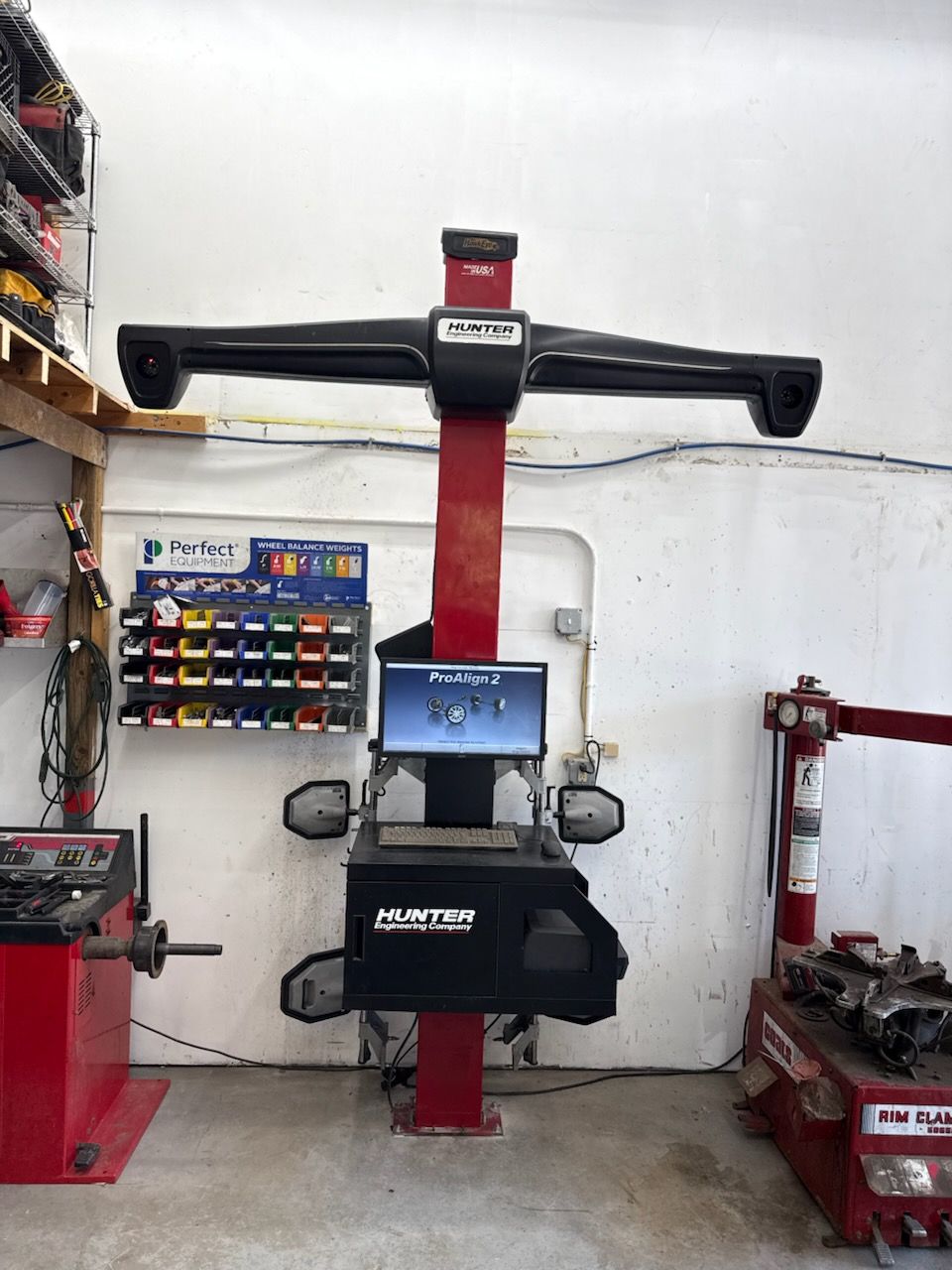 Tire on a balancing machine in a garage; black tire, silver rim, red and gray machine.
