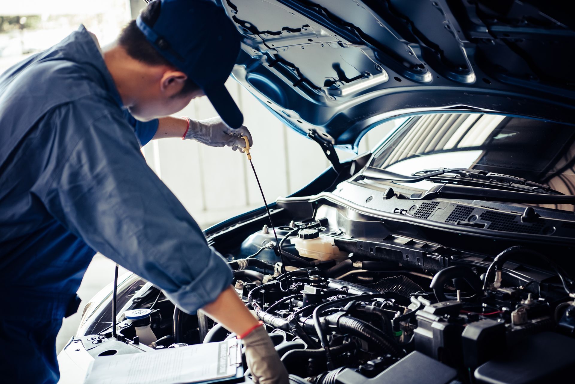 Mechanic checking engine oil with dipstick, car hood open in garage.