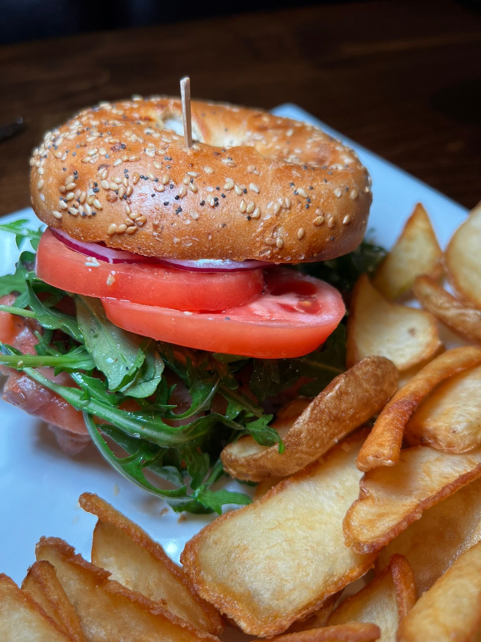Sesame bagel sandwich with lettuce and tomato, served with potato wedges on a white plate.