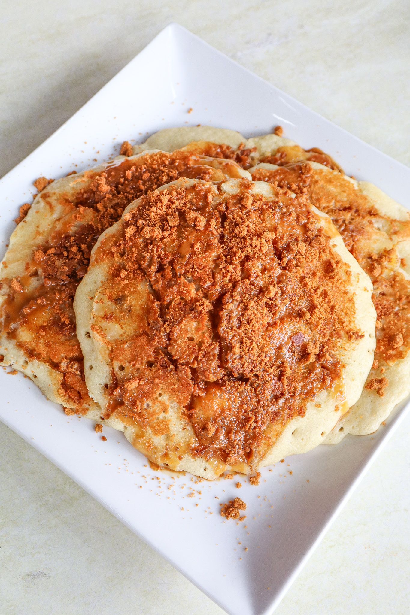 Plate of pancakes topped with cinnamon and sugar on a white square plate.