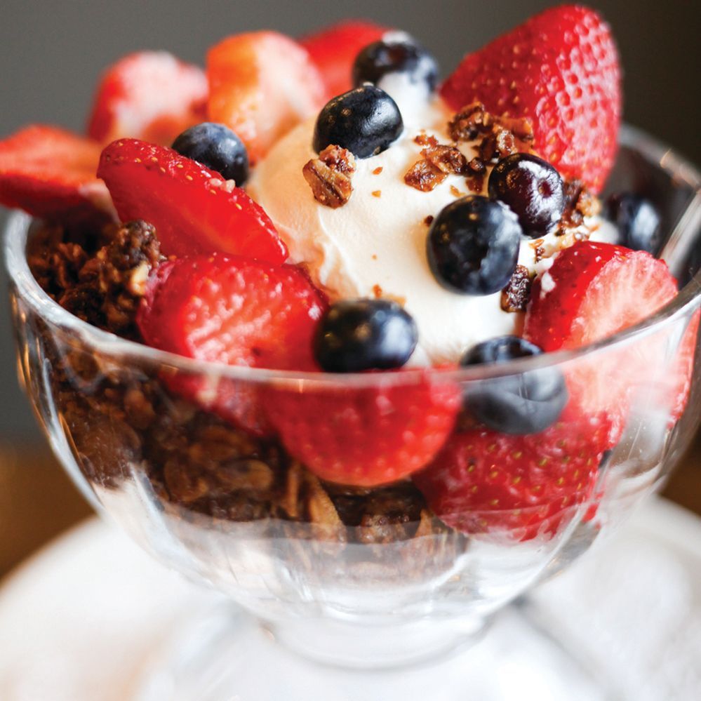 Glass bowl of granola with yogurt, strawberries, and blueberries