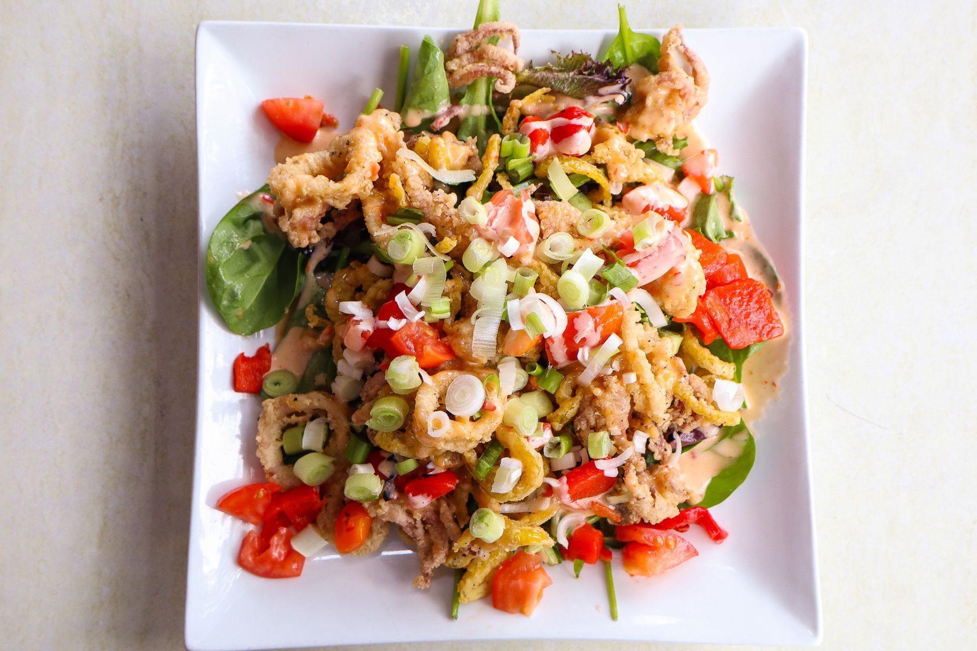Colorful salad with greens, strawberries, nuts, and crumbled cheese on a white square plate