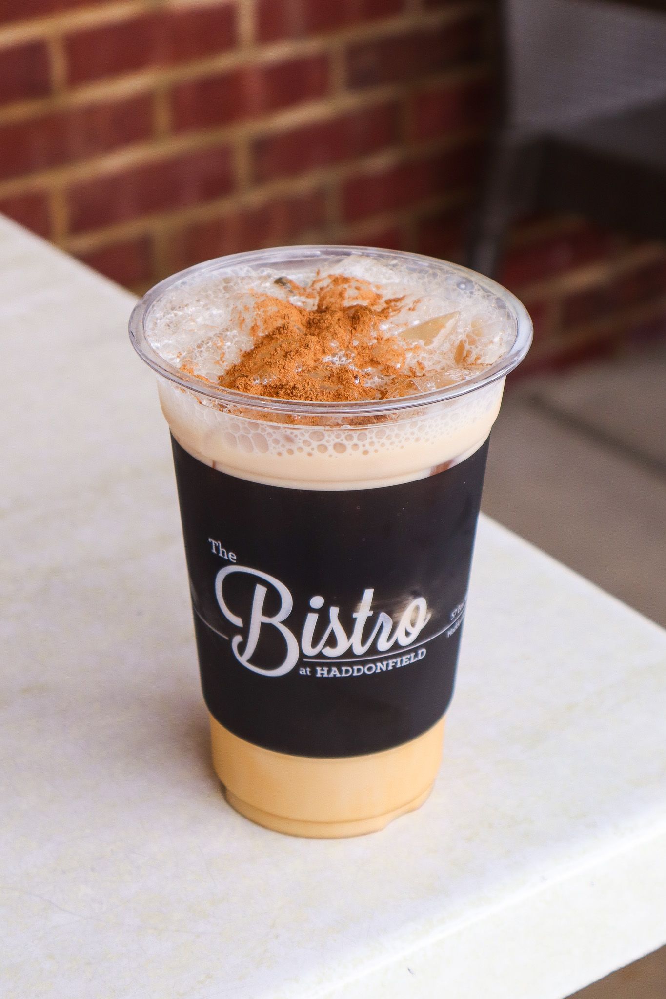 Iced coffee in a clear plastic cup with a black sleeve on a table, topped with cinnamon.