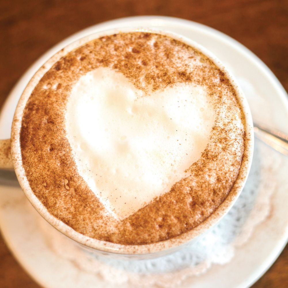 Top-down view of a cappuccino with heart-shaped latte art in a white cup and saucer