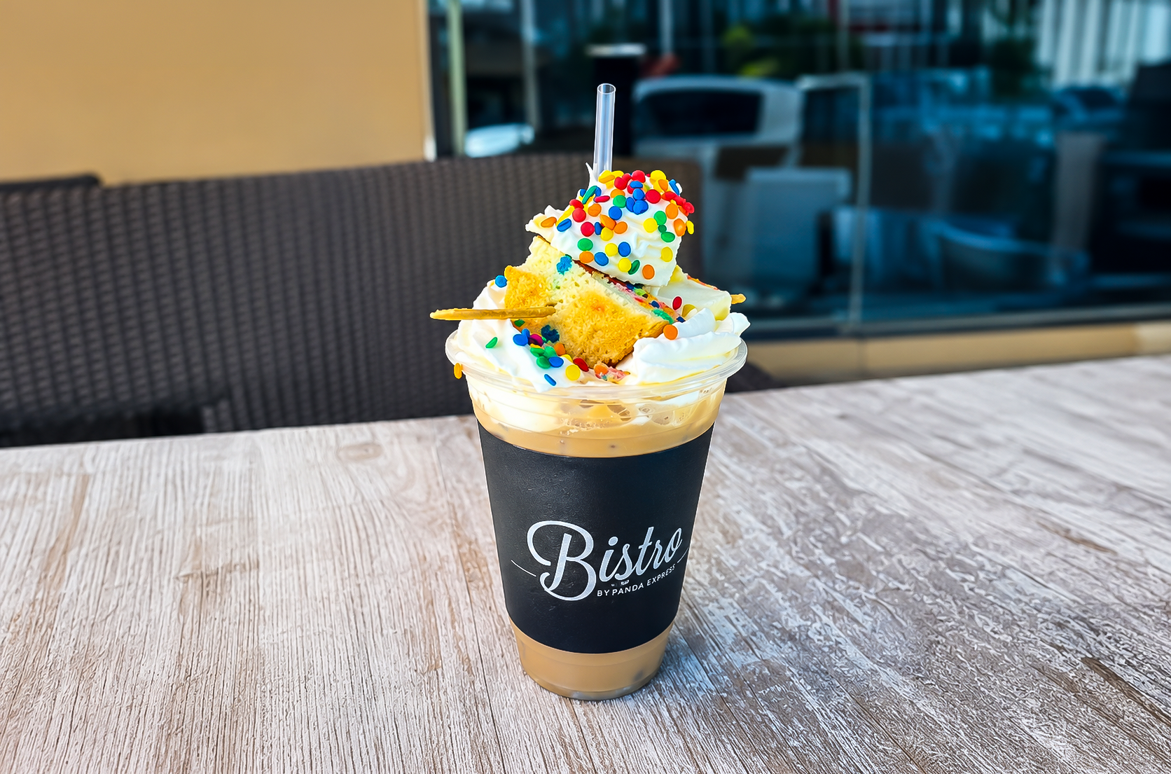 Whipped coffee drink topped with sprinkles and a straw on a wooden table in a cafe