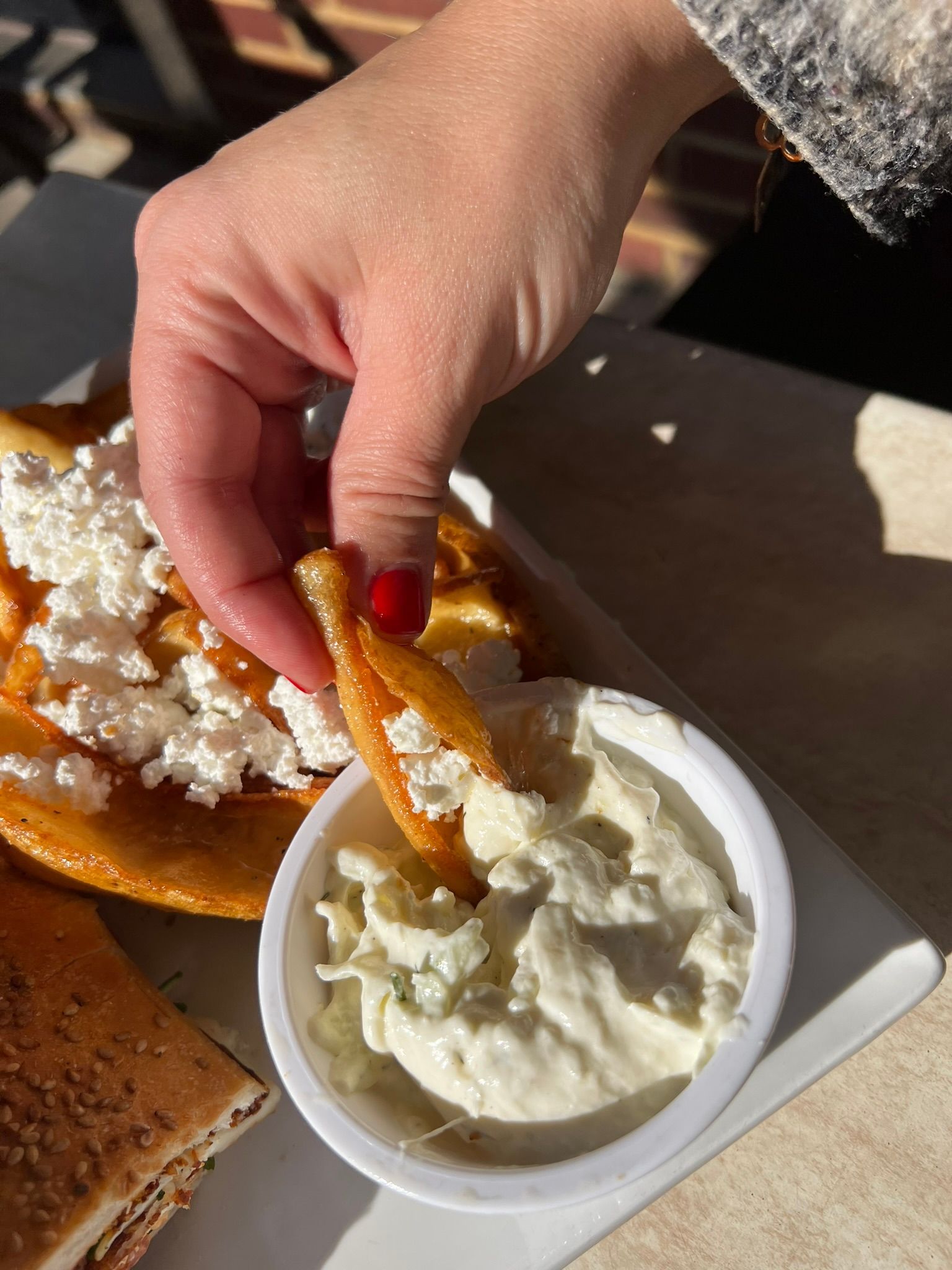 Hand dipping an orange chip into a cup of white dip beside a plated meal