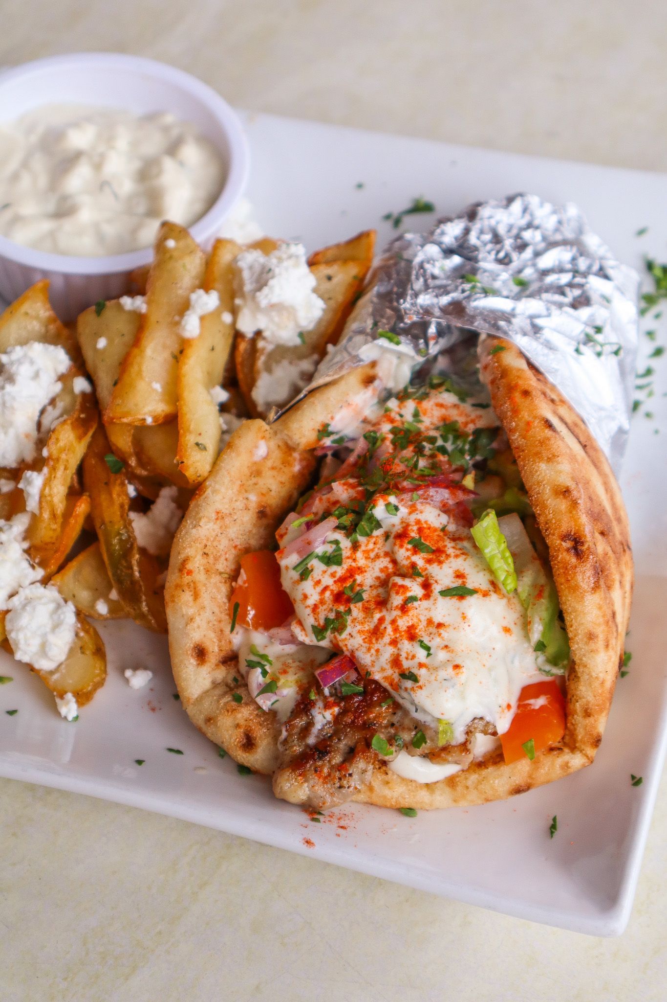 Greek-style wrap with fries and tzatziki on a white plate, topped with herbs and red seasoning
