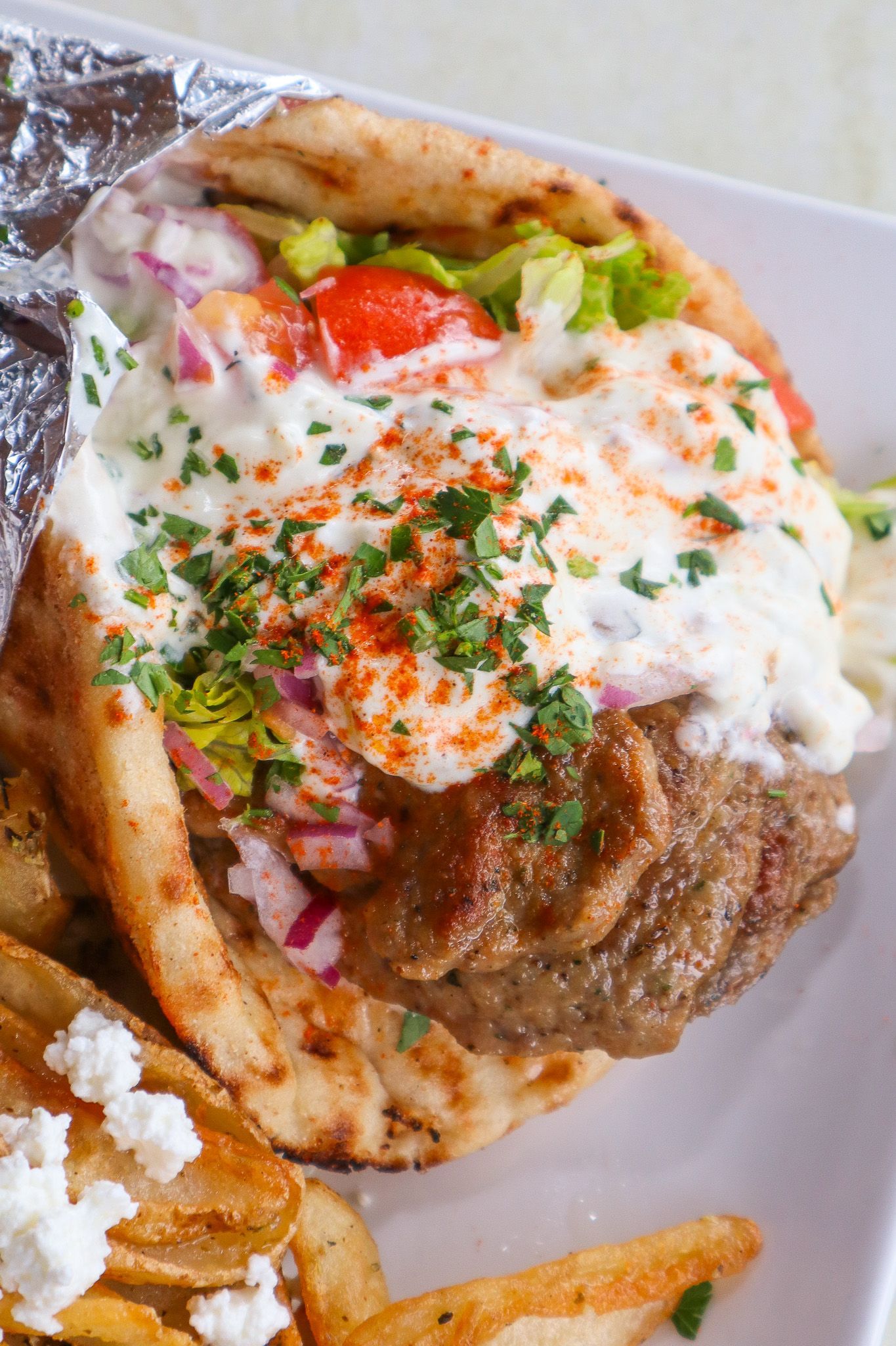 Close-up of a loaded gyro wrap with meat, tomato, onions, and white sauce on flatbread