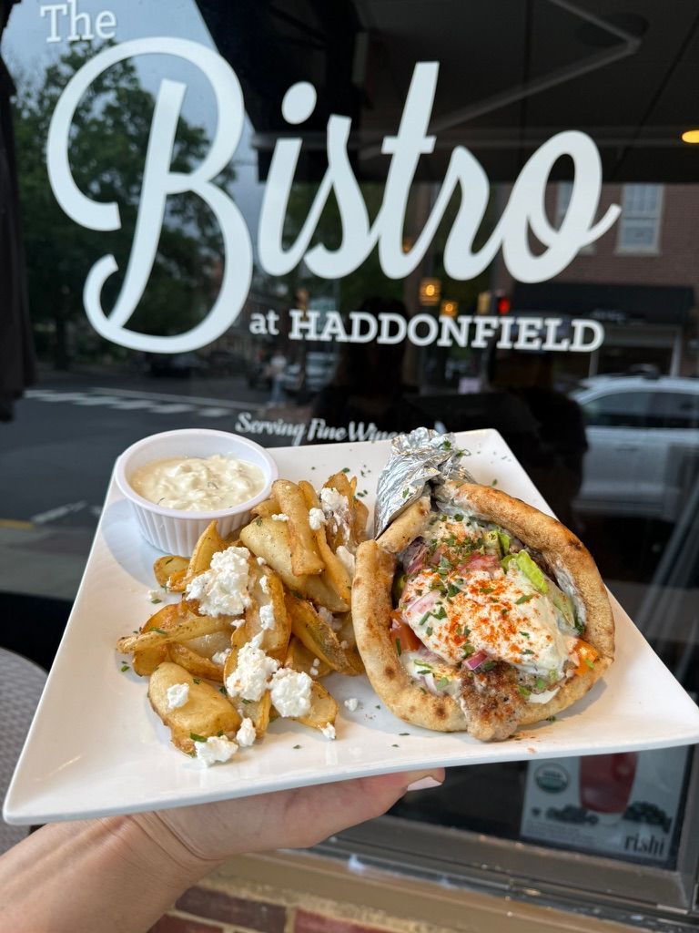 Hand holding a plate of seafood in front of The Bistro at Haddonfield window sign