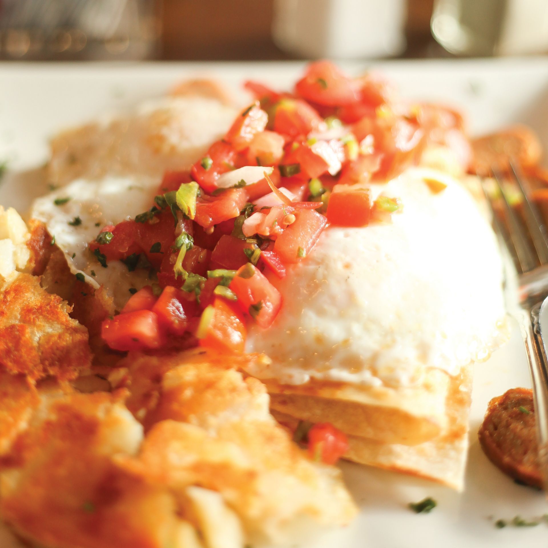 Baked dish topped with melted cheese and diced tomatoes, served with crispy golden pieces on a white plate