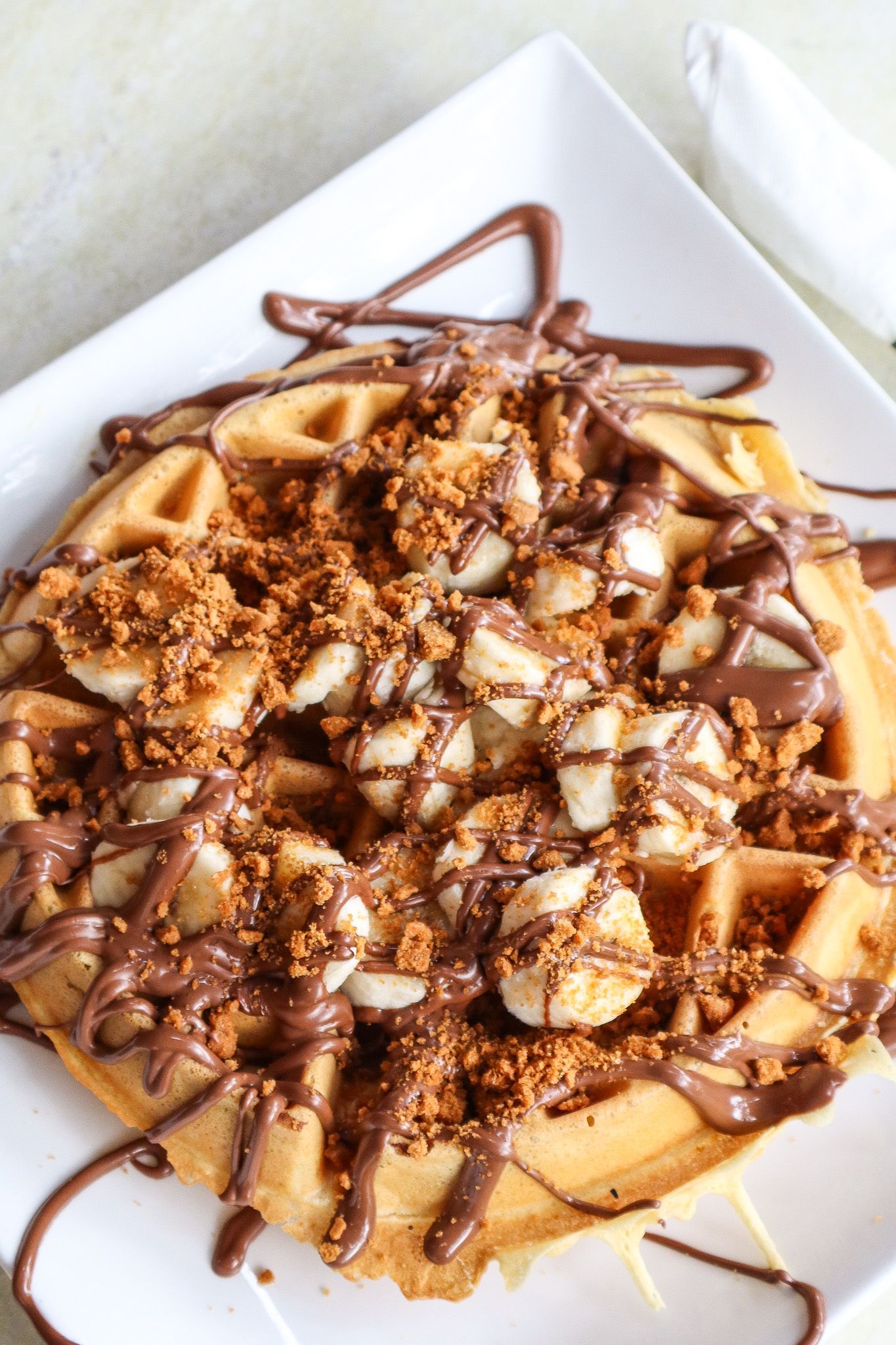 Chocolate-drizzled crêpe topped with sliced bananas on a white plate