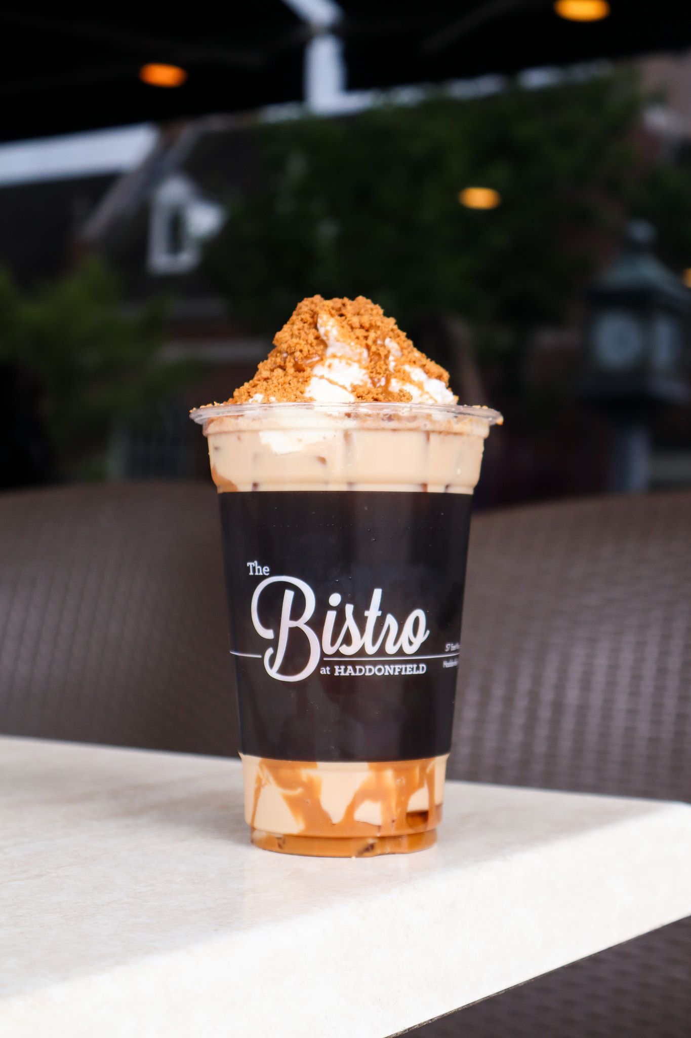 Iced caramel coffee in a clear cup with whipped cream on a table, blurred café background