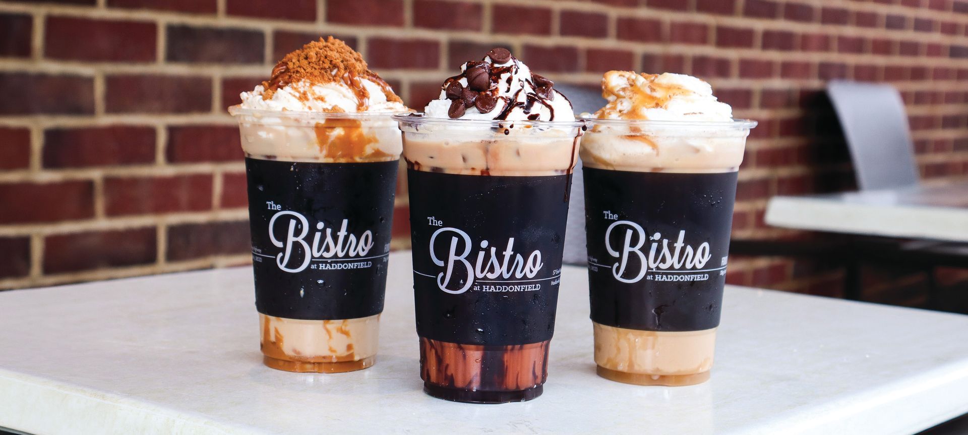 Three iced coffee drinks topped with whipped cream and chocolate drizzle on a table
