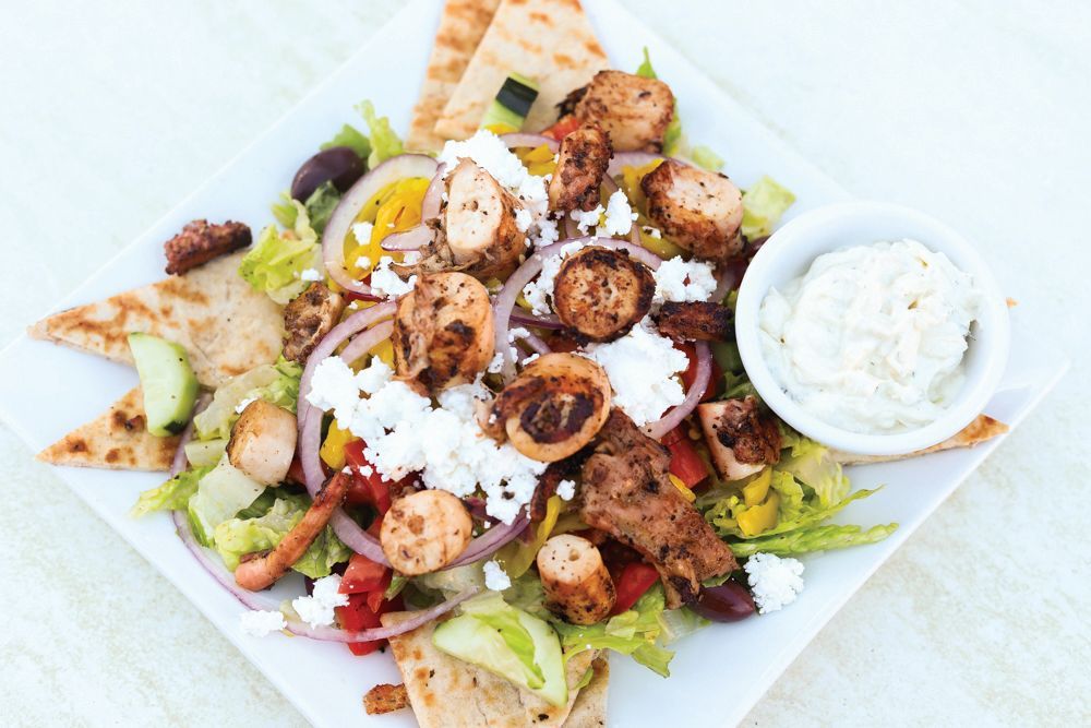 Grilled chicken salad with pita triangles and a bowl of creamy dressing on a white plate