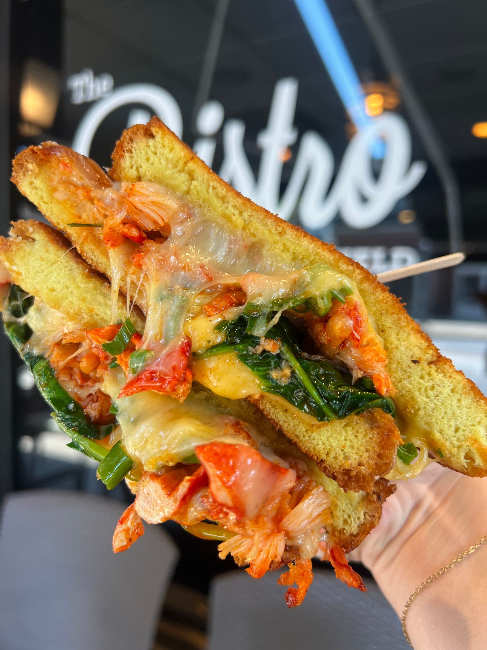 Close-up of a grilled sandwich with melted cheese, tomato, and greens held in a hand