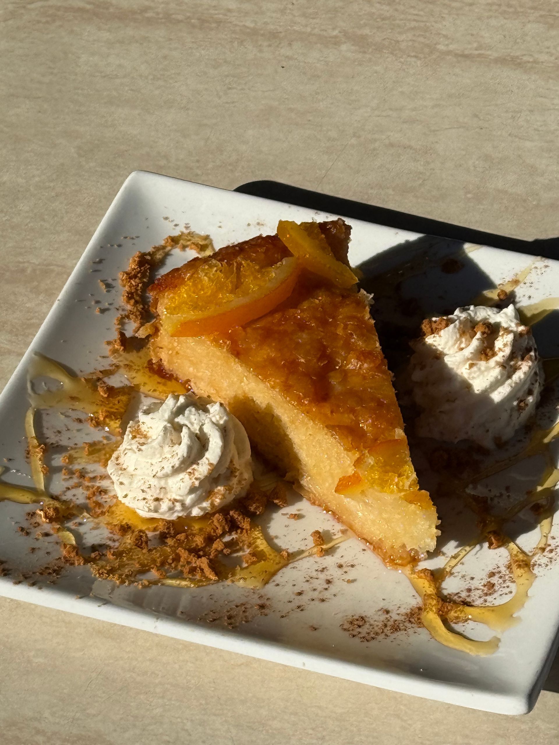 Slice of peach tart with whipped cream on a square white plate, drizzled with caramel.