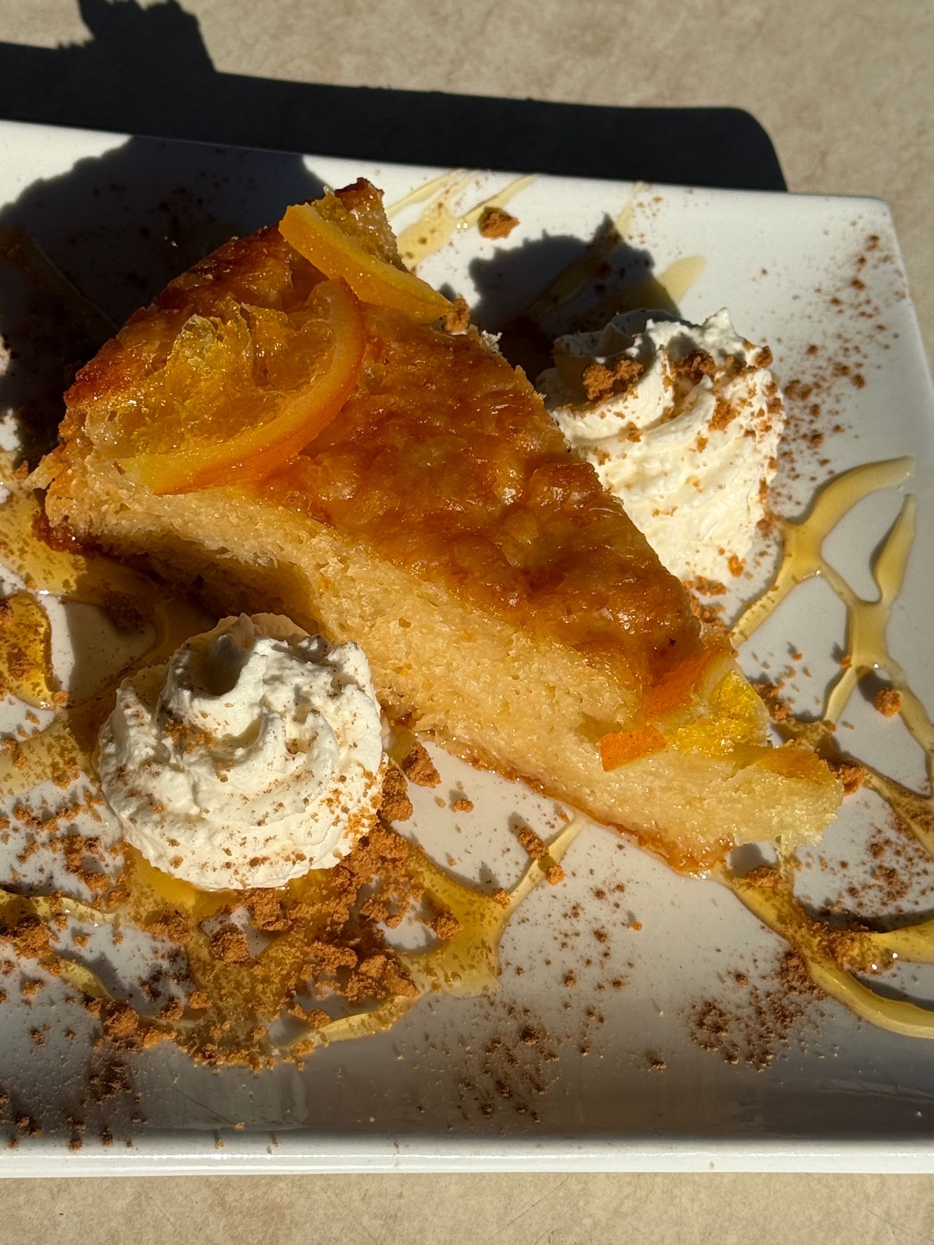 Slice of caramel cake on a white plate with whipped cream and caramel drizzle, with crumbs scattered around