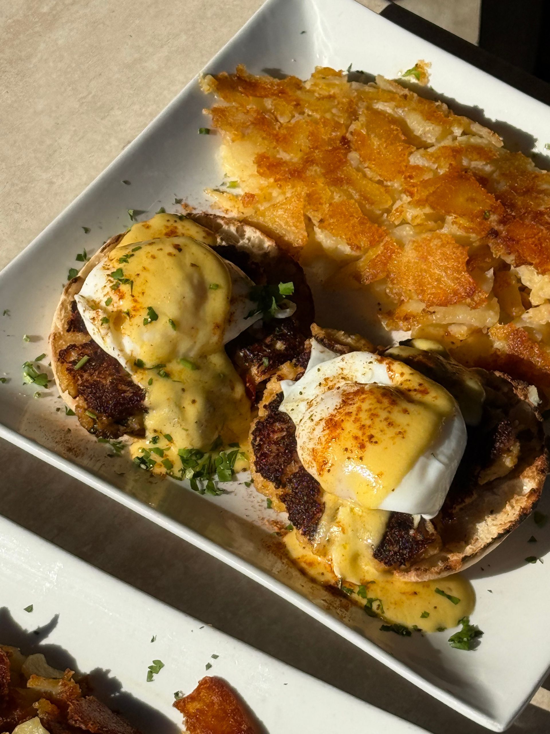 Two burgers topped with fried eggs on a white plate, with a crispy side on top.