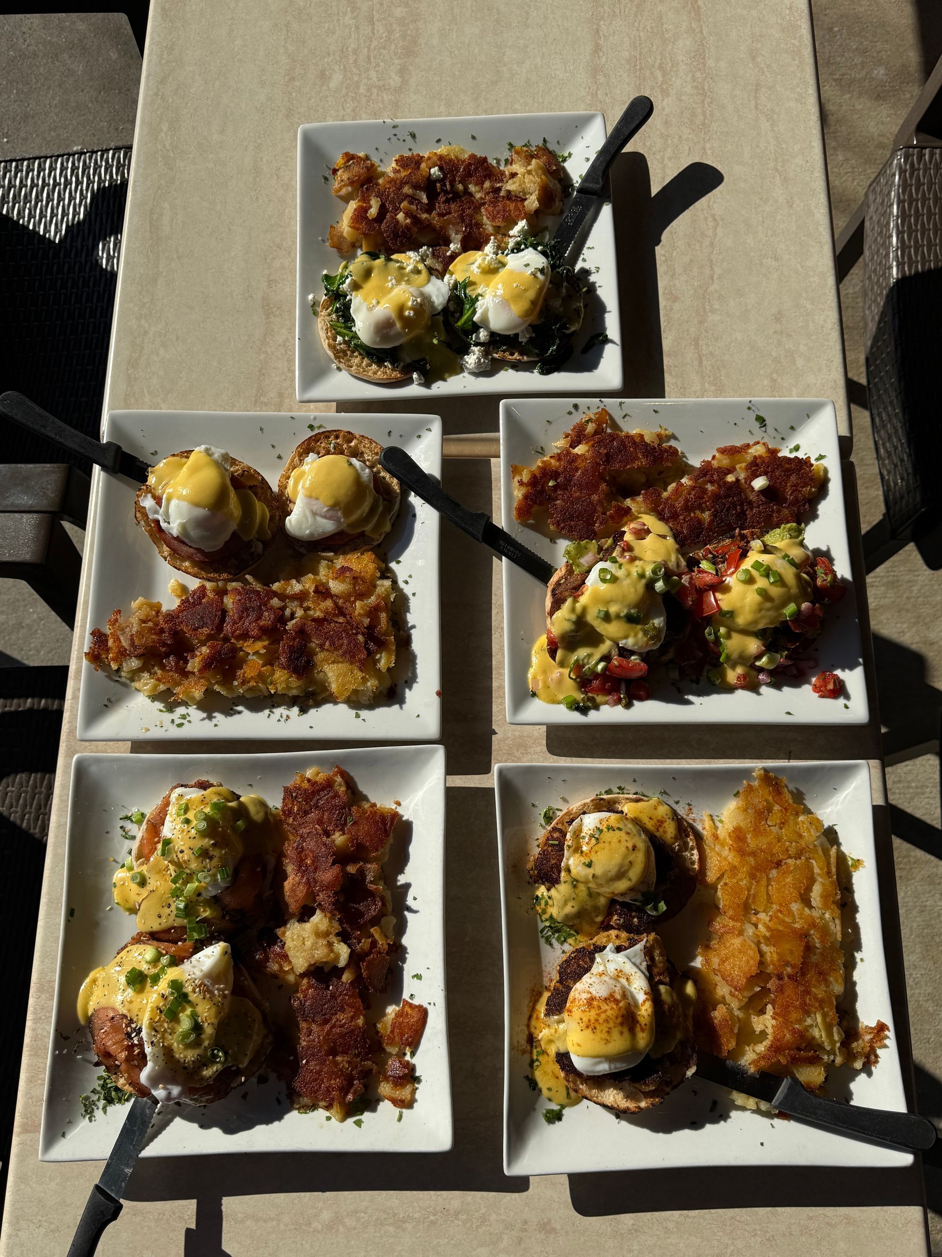 Five plates of assorted sushi rolls with chopsticks on a gray table.
