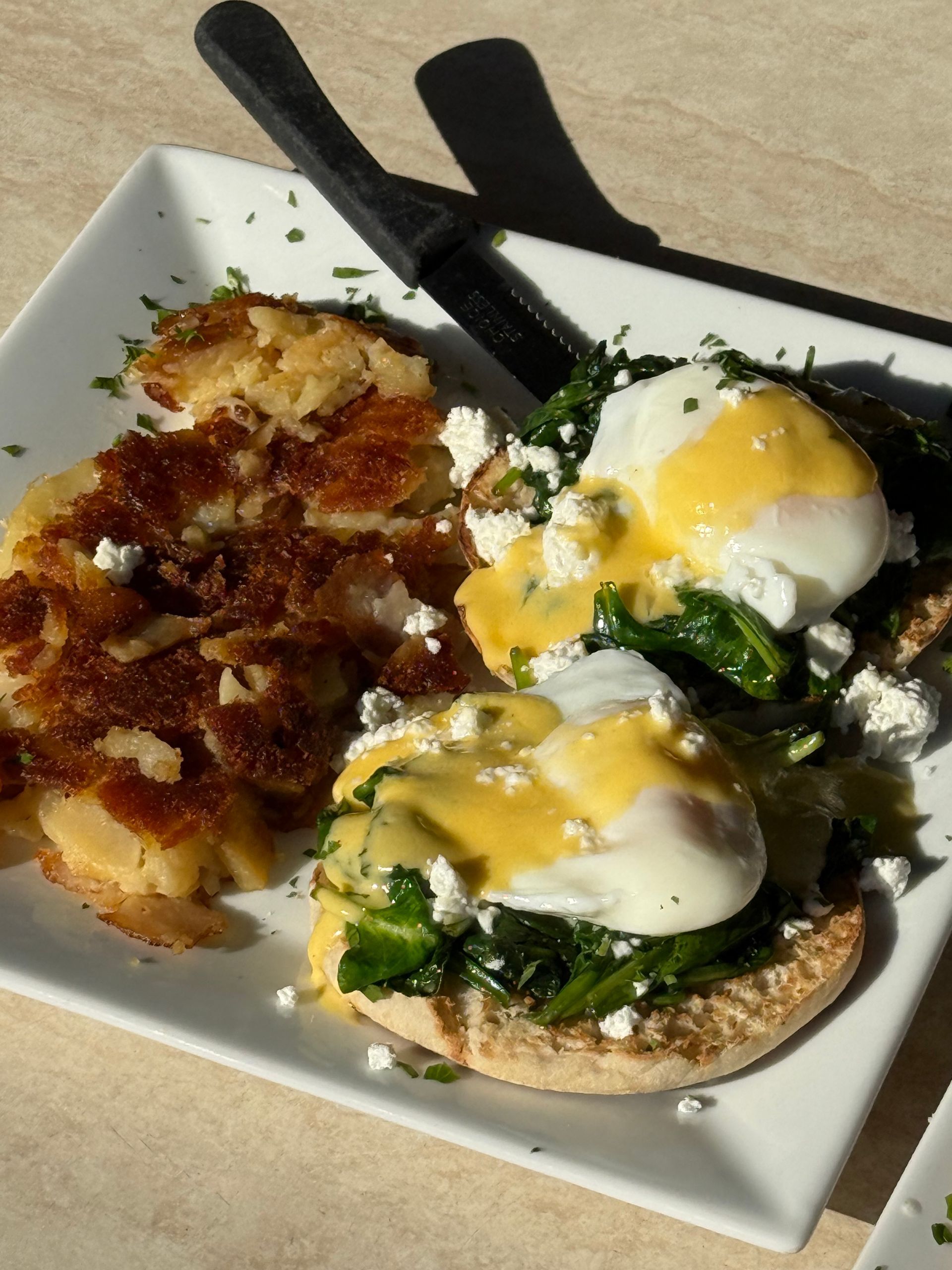 Brunch plate with eggs benedict, spinach, and hash browns on a white plate