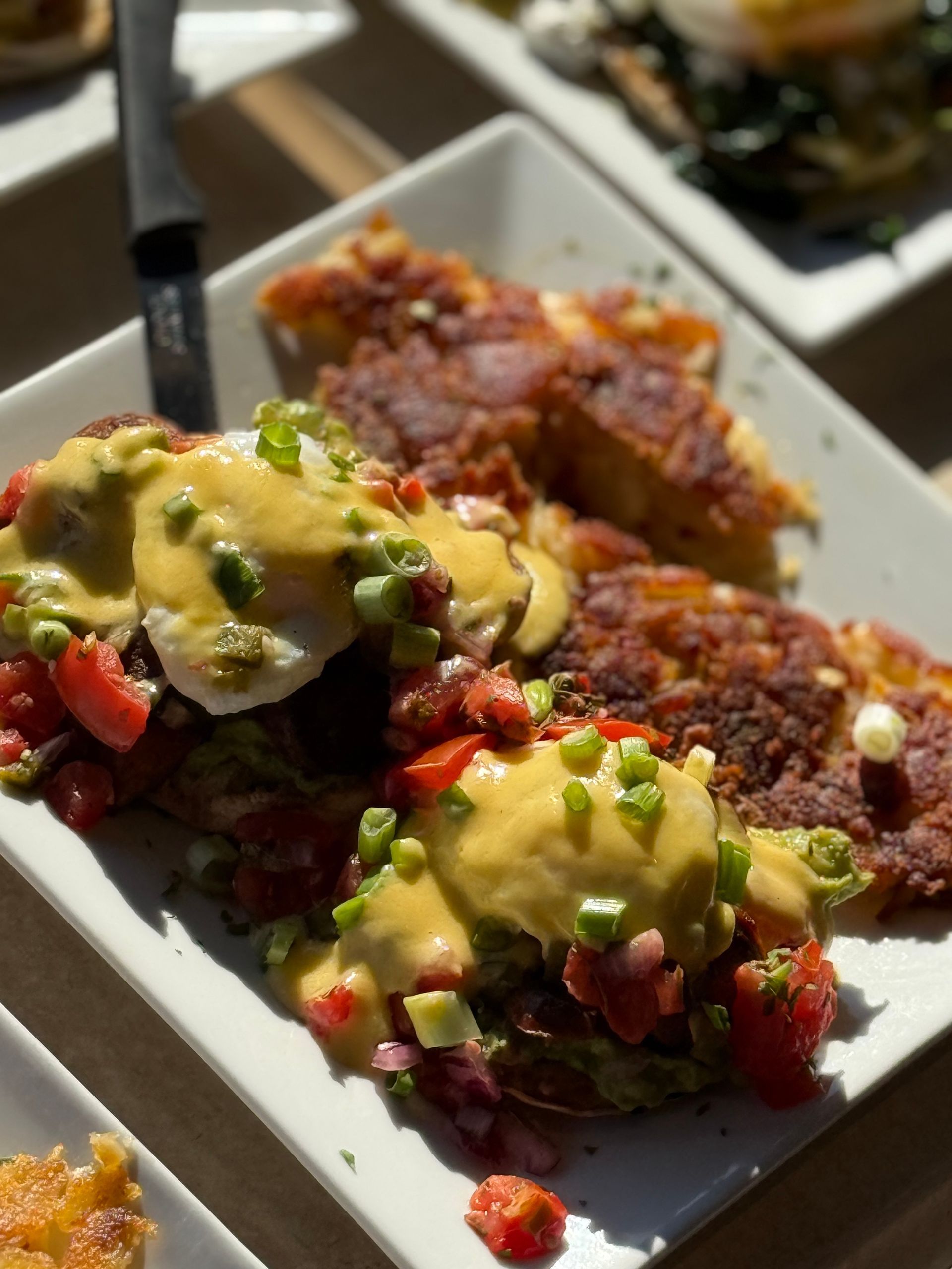 Plated nachos topped with guacamole, salsa, cheese, and diced vegetables on a restaurant table
