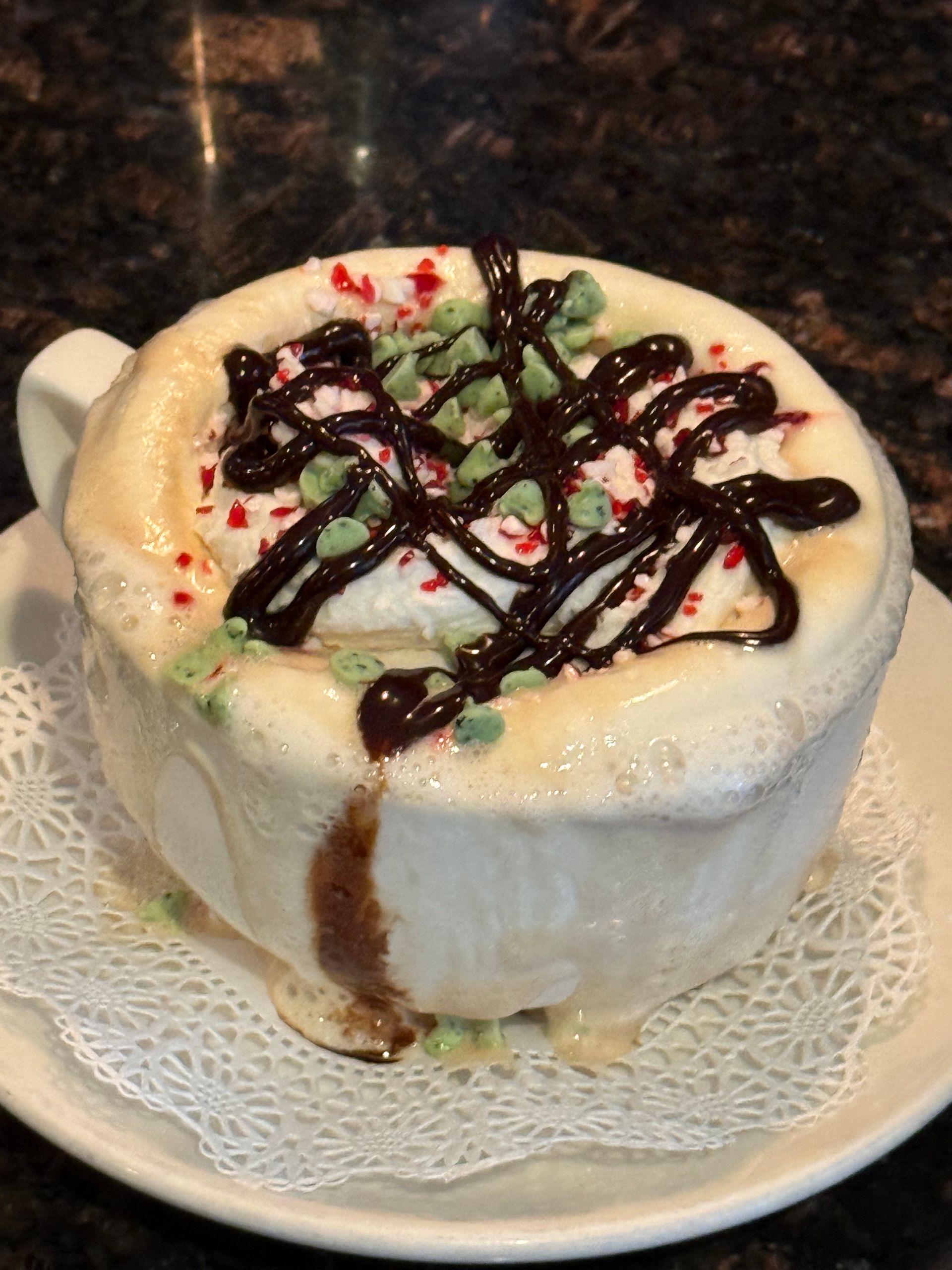 Ice cream dessert drizzled with chocolate and red syrup on a white plate with a doily