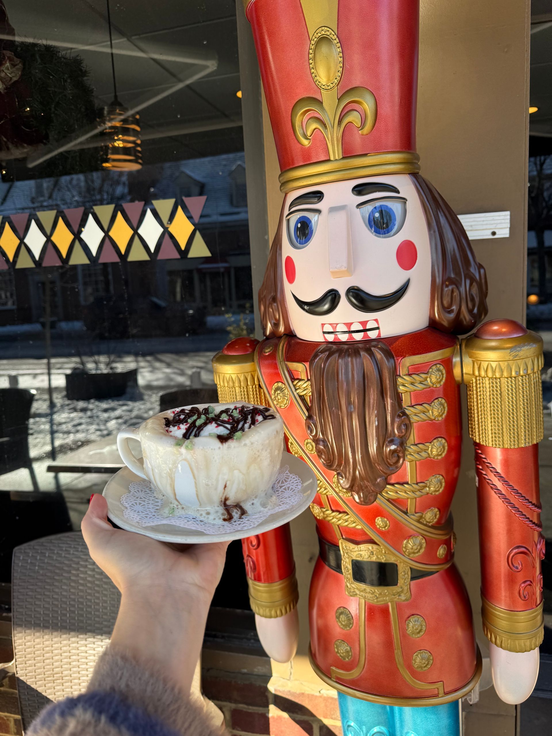 Hand holding a dessert cup beside a colorful toy soldier statue outside a restaurant
