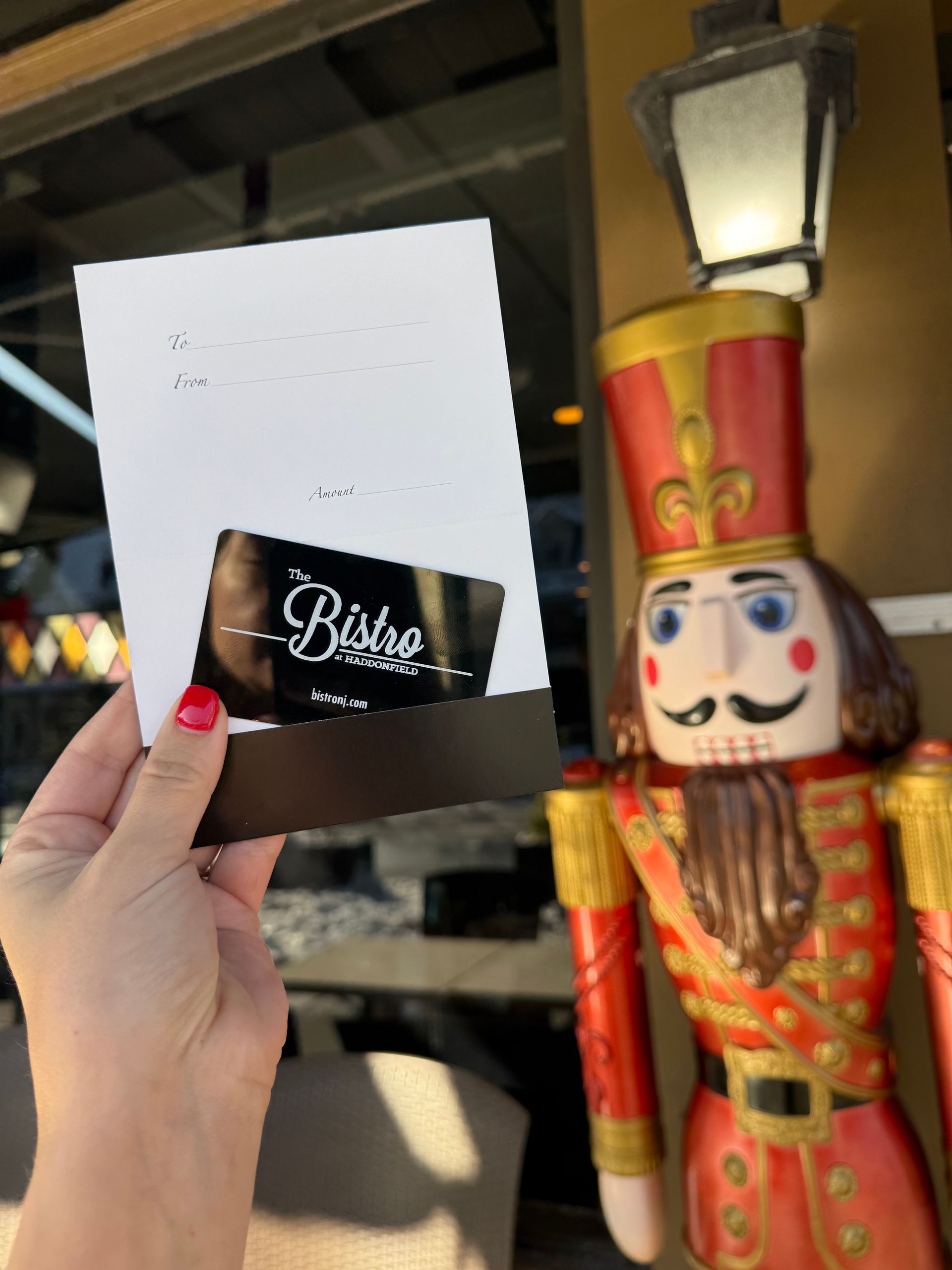 Hand holding a black Bisou gift card beside a red-and-gold nutcracker decoration in a shop setting